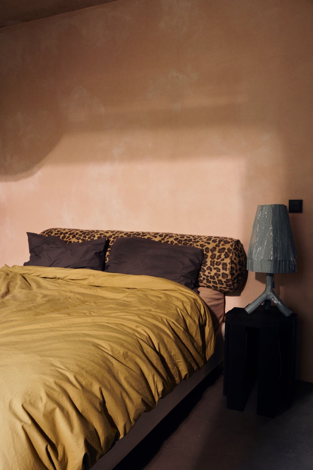 Mustard yellow bedding styled with HKLIVING leopard print bolster cushion against a terracotta pink wall