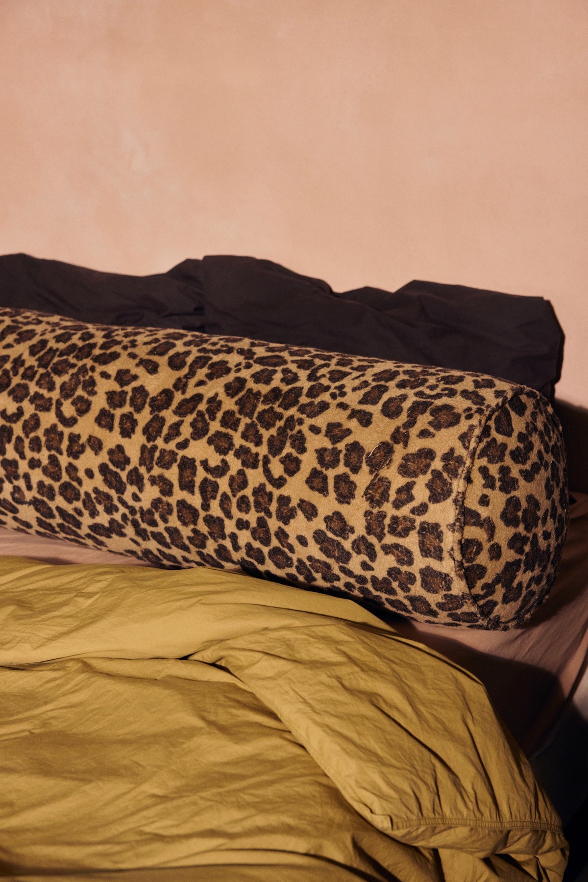 Close-up of HKLIVING leopard print bolster cushion on a bed with mustard yellow and brown bedding