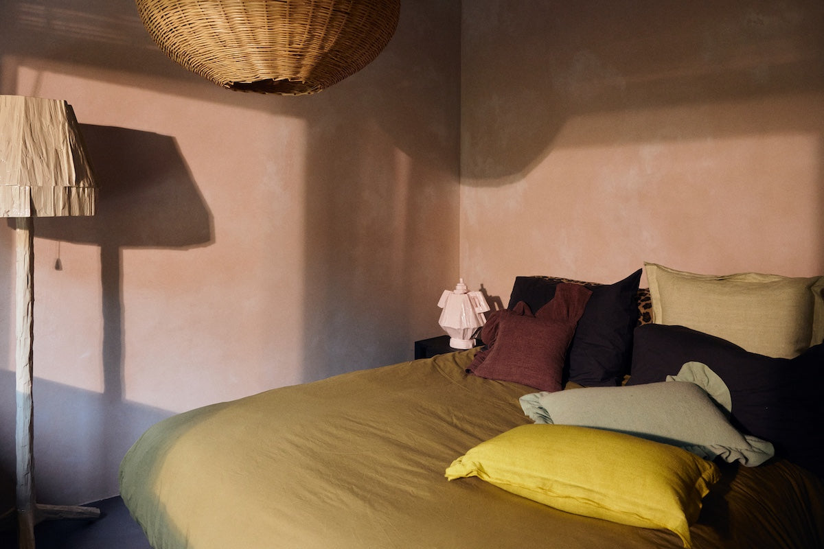 Lemongrass yellow linen cushion styled on a bed with mixed colour cushions