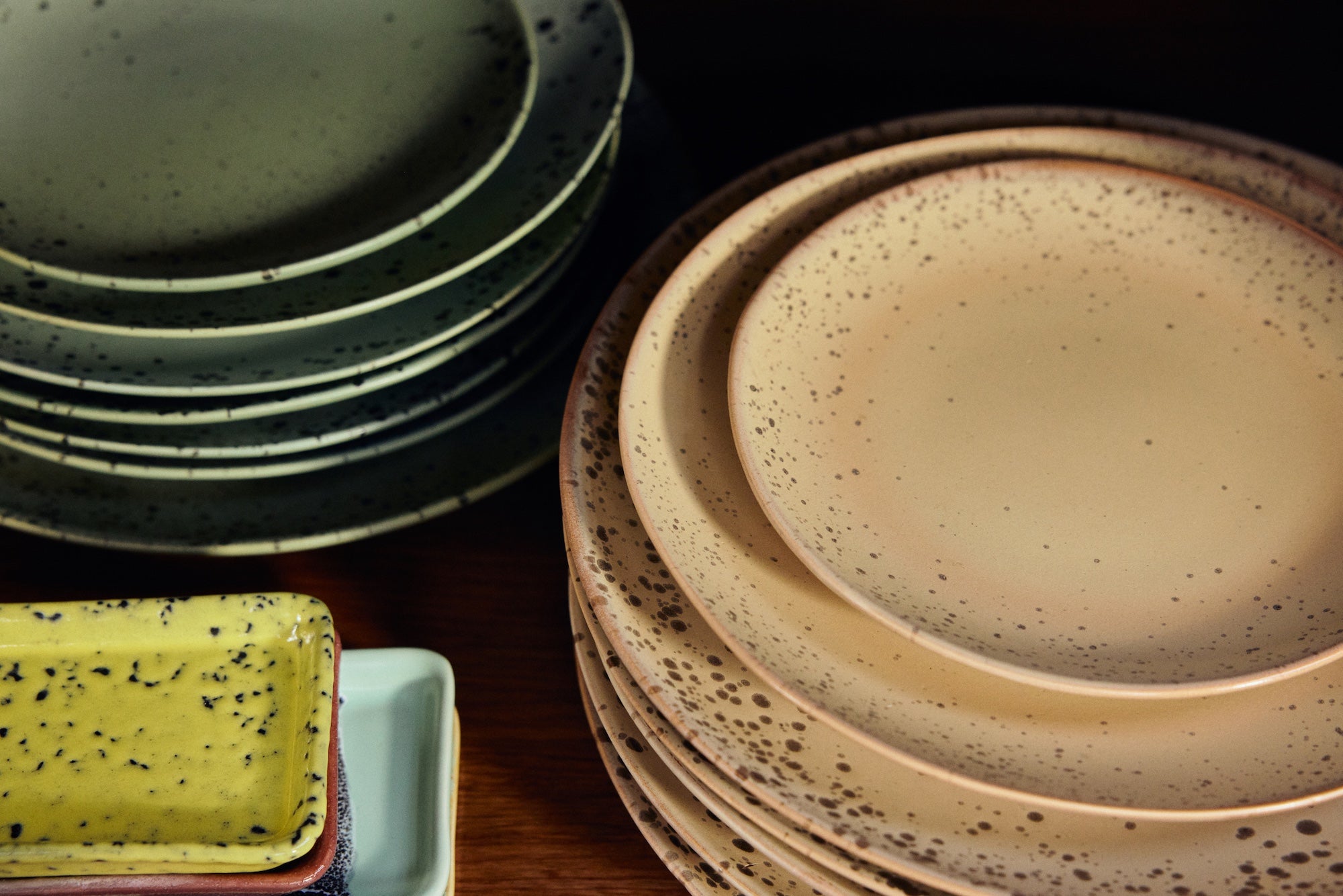 Close-up of stacked HKLIVING 70s Ceramics plates in Grit and other colourways on a wooden surface