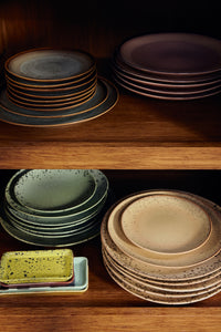 Stacked HKLIVING 70s Ceramics plates in dark grey, plum, sage green and sandy beige grit glazes on wooden shelving