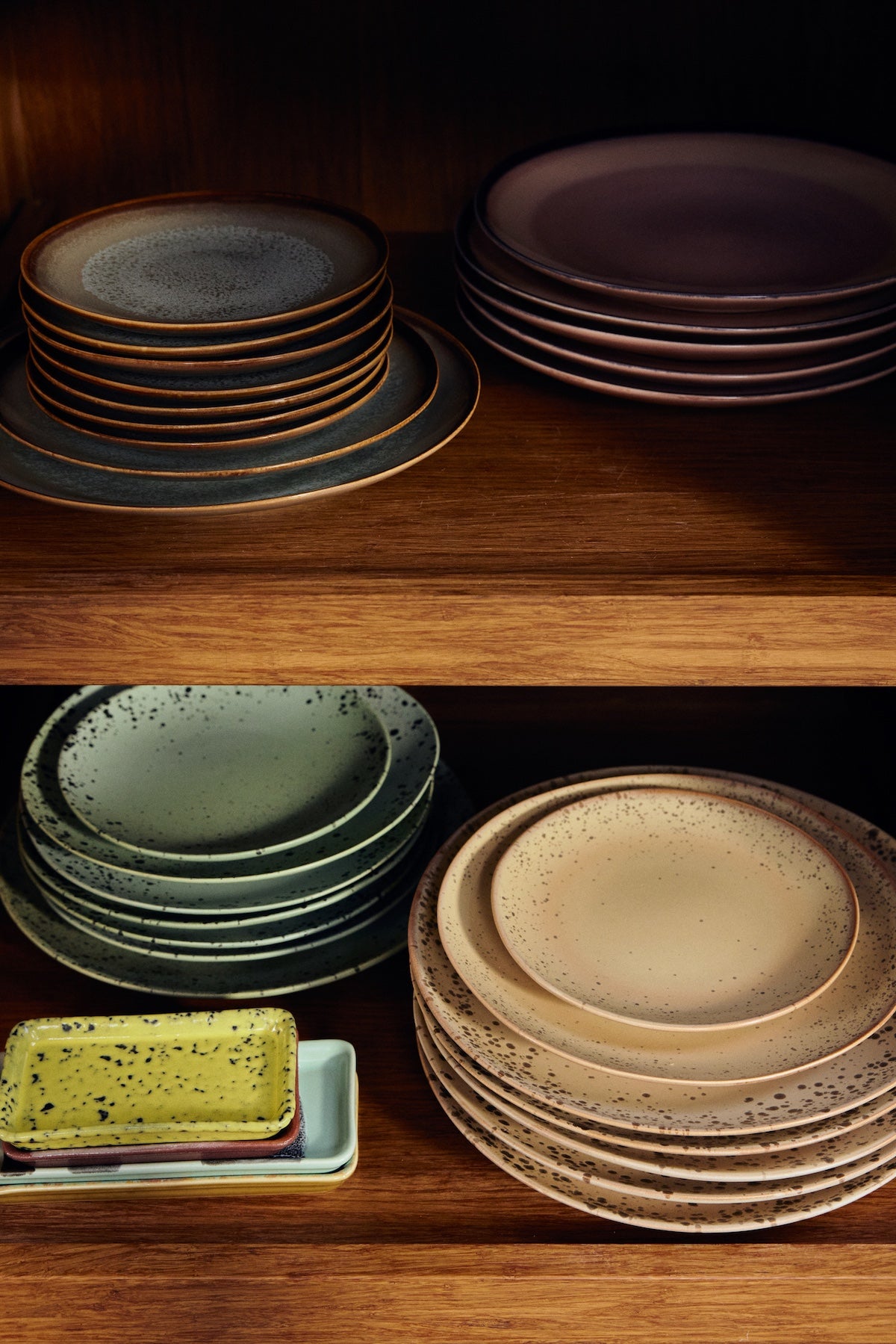 Stacked HKLIVING 70s Ceramics plates in dark grey, plum, sage green and sandy beige grit glazes on wooden shelving