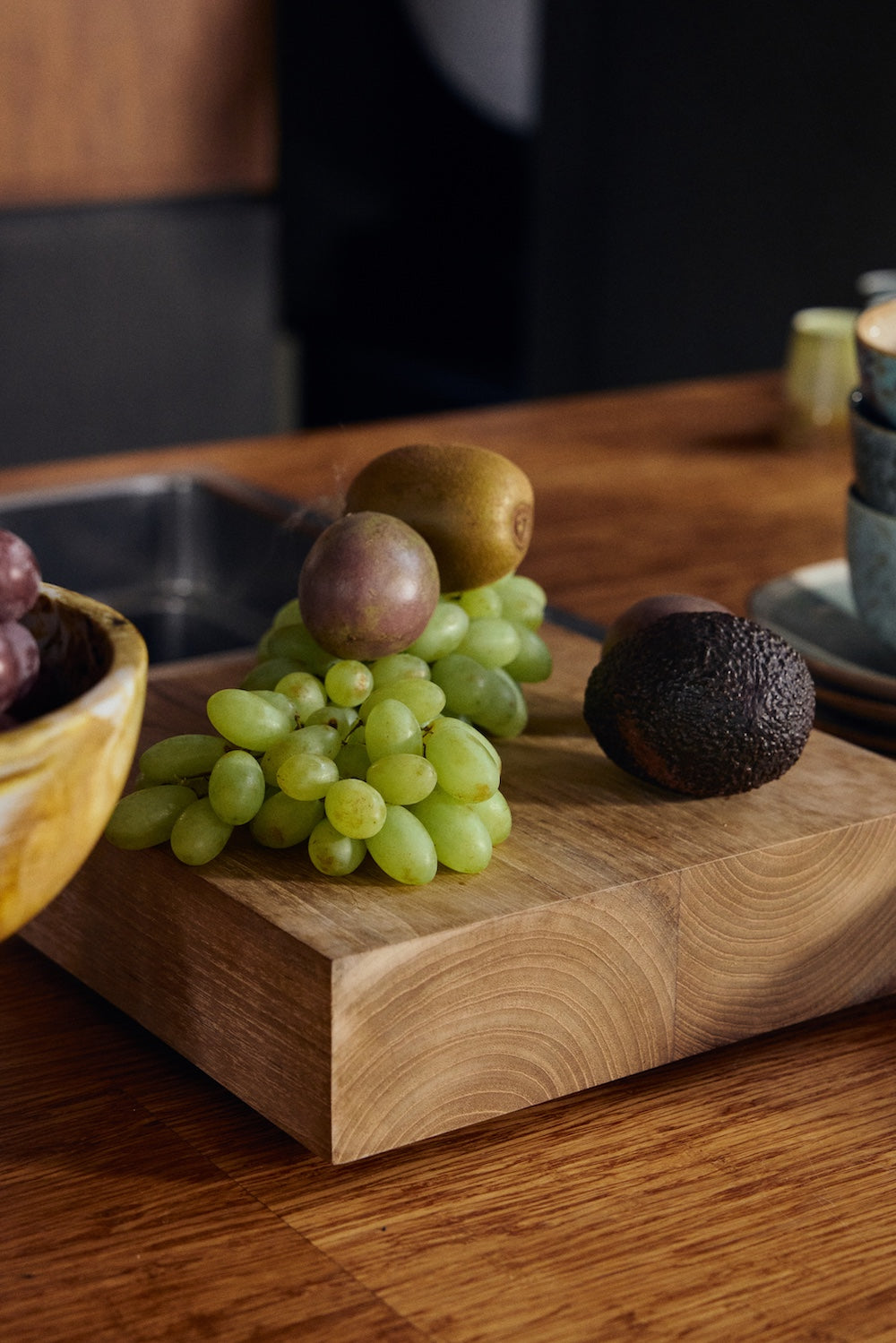 Grapes, a kiwi and an avocado arranged on top of the large HKLIVING teak cube, styled on a wooden kitchen counter