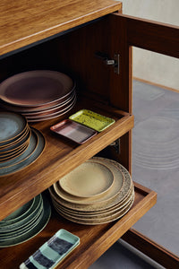 Open wooden cabinet displaying HKLIVING 70s Ceramics plates and trinket trays in multiple colourways including sandy beige grit