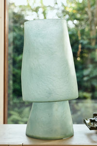 HKLIVING Glassfibre Table Lamp in Petrol Blue close-up on a surface with lush garden backdrop showing mint green colour