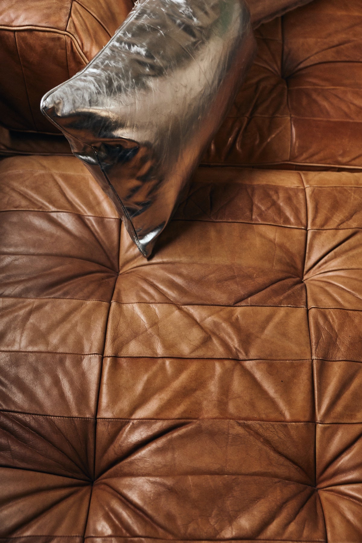 Silver faux leather cushion resting on tan leather sofa upholstery