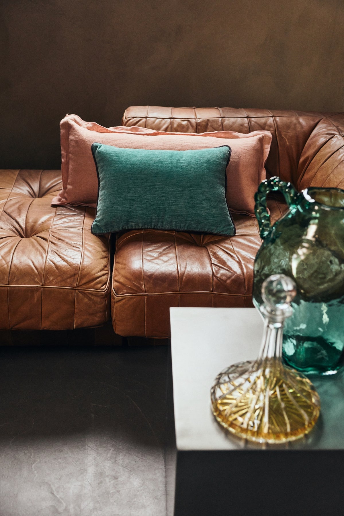 Dusty peach linen cushion styled with a green velvet cushion on a leather sofa
