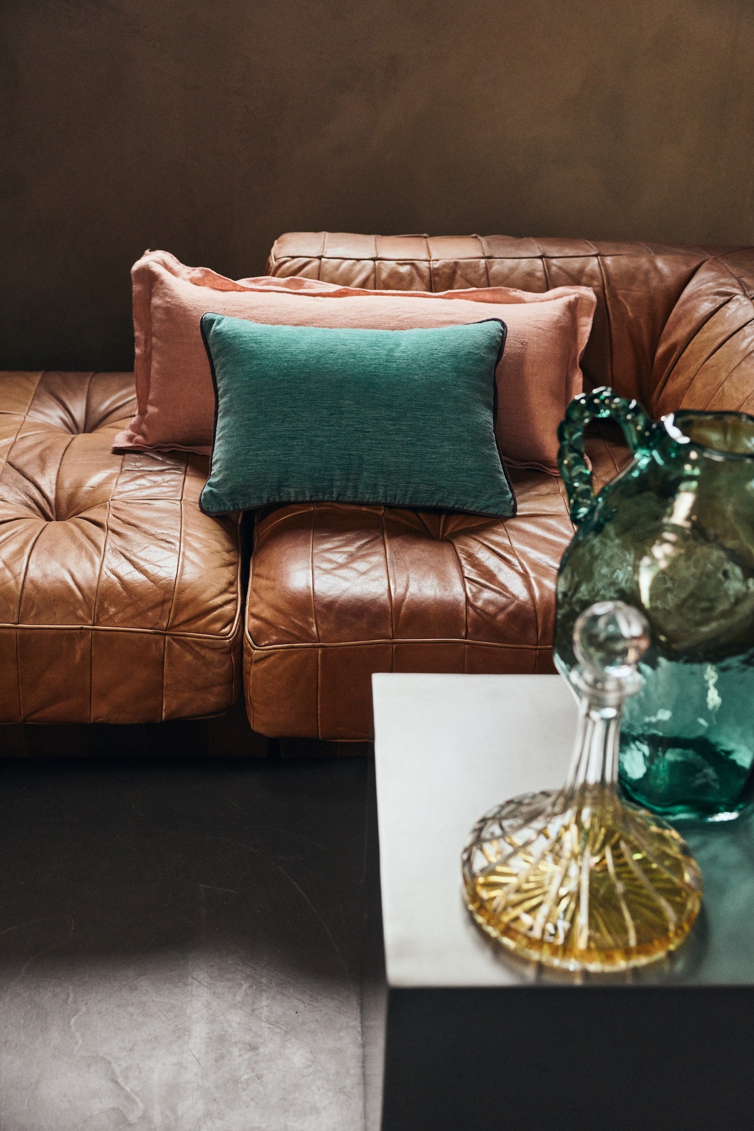 Dusty peach linen cushion styled with a green velvet cushion on a leather sofa