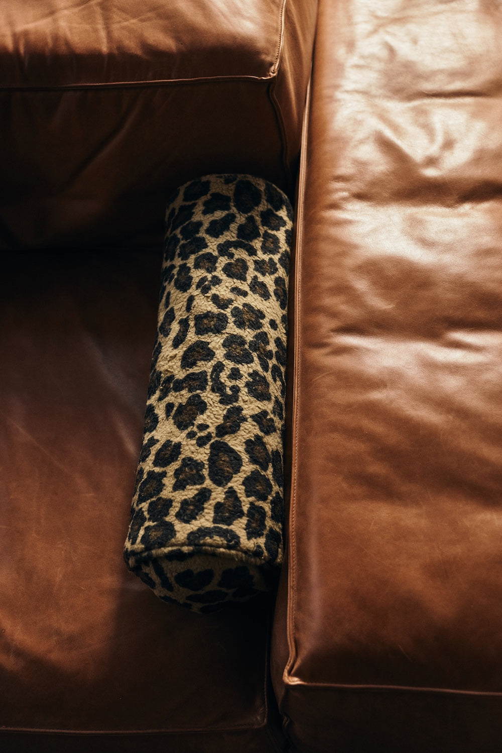 Close-up of the HKLIVING Panther bolster cushion resting in the corner of a brown leather sofa