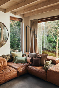 Leather corner sofa in a bright living room styled with an assortment of cushions, including the HKLIVING Panther bolster in leopard print