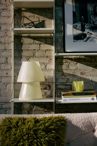 HKLIVING Glassfibre Table Lamp in Off White on a wall-mounted shelf alongside books and a moss green cushion