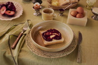 Breakfast table styled with HKLIVING 70s Ceramics sandy grit bowl and plate, toast and jam, set on an olive green tablecloth