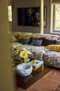 Cloud Bowl in Sky Blue on a glass coffee table in a light, plant-filled living room with a floral corner sofa