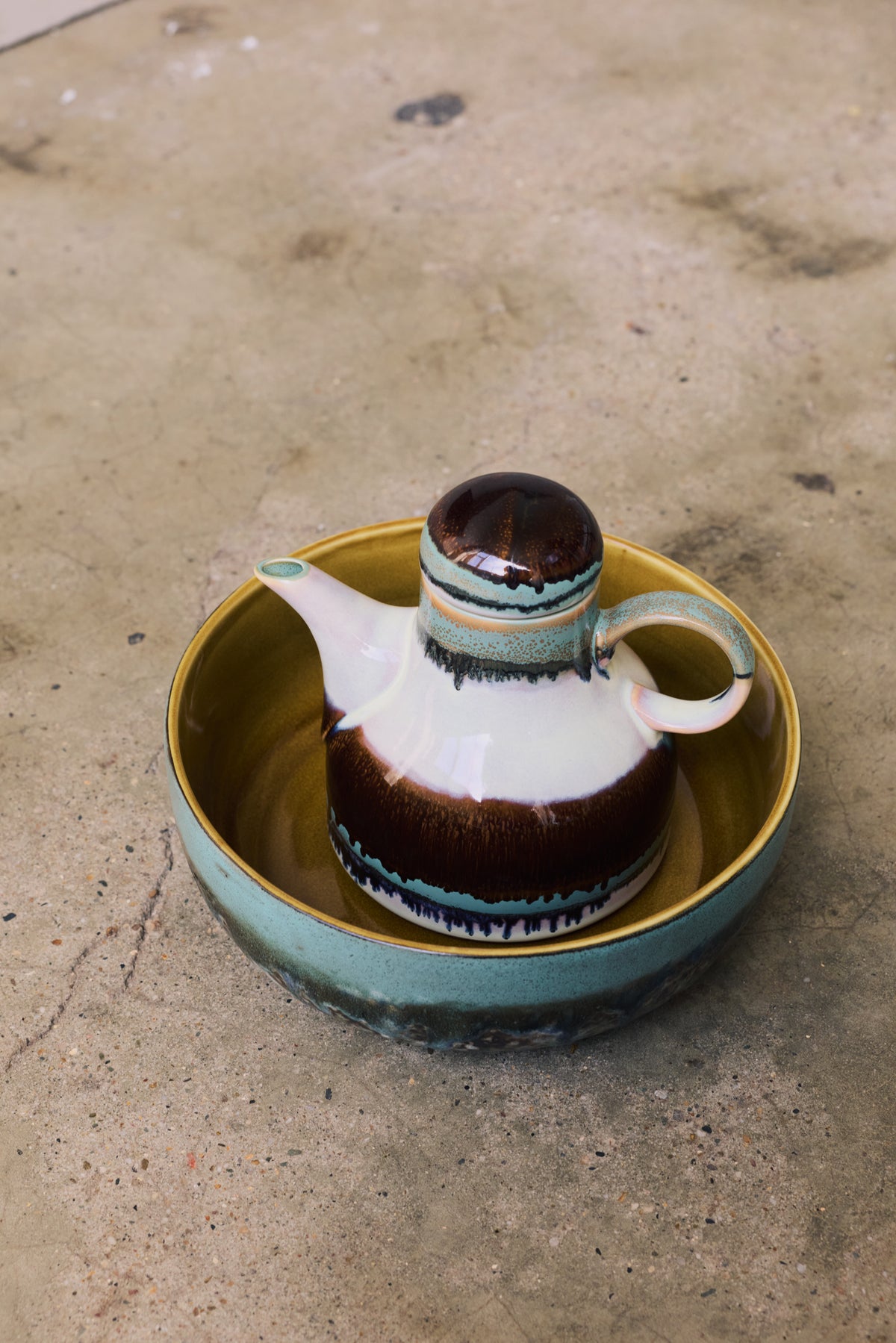 70s Ceramics Coffee Pot in Chocolate displayed inside a turquoise glazed bowl on a concrete surface