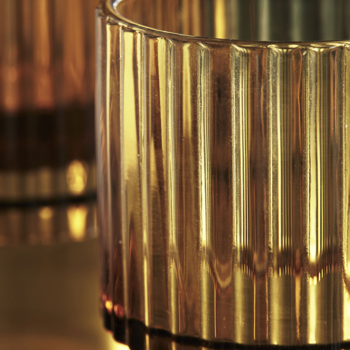 Close-up of the fluted ribbed amber glass on the House Doctor Rills tumbler, catching warm light for a cosy table feel