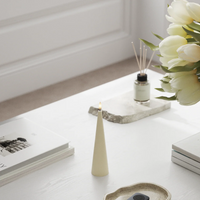 Decorative items on a white surface including a candle, books, and a vase with flowers.