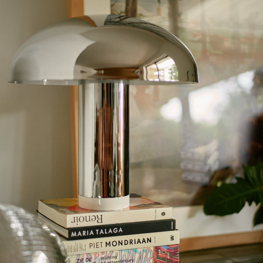 shiny chrome mushrrom lamp standing on a stack of a few books reflecting images of other hkliving products from its background