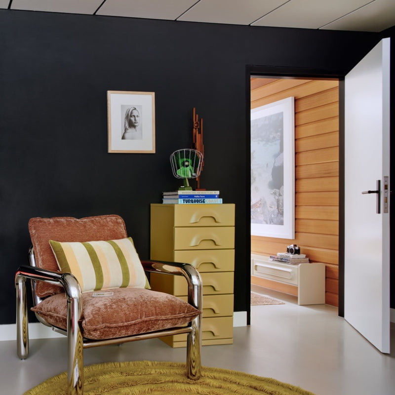 a home office with a funky brown velvet armchair with think chrome tubes for its legs and arm rests and a drawer unit with the large sulpture stood on it