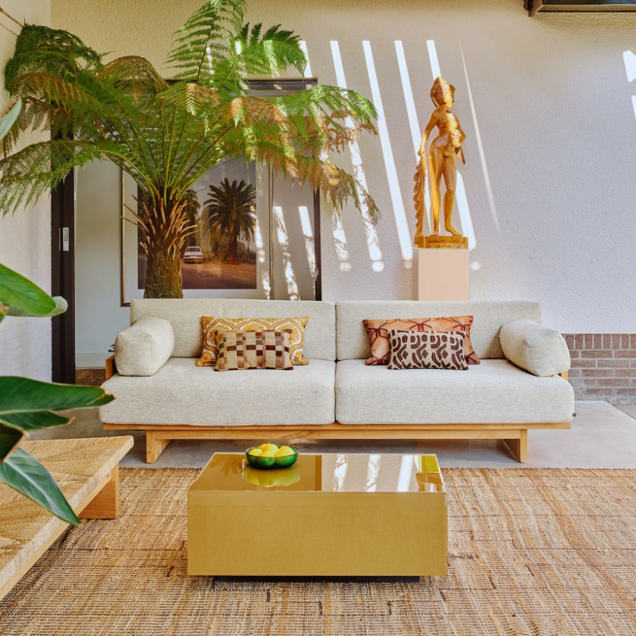 living room set up with a deep, woven sofa, a wooden indonesian sculpture in the background that almost looks golden in the sunlight