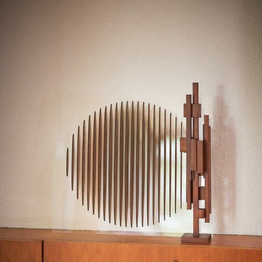 the medium scultpure on a wooden unit with a circular wooden piece behind it on the wall