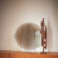 the medium scultpure on a wooden unit with a circular wooden piece behind it on the wall