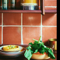 a kitchen scene with terracotta tiles, a quiche on a plate, and the begginings of a salad in a sunshine salald bowls