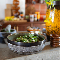 salad bowl sat on a breeze block wall of a kitchen with dinner making activity going on in the background