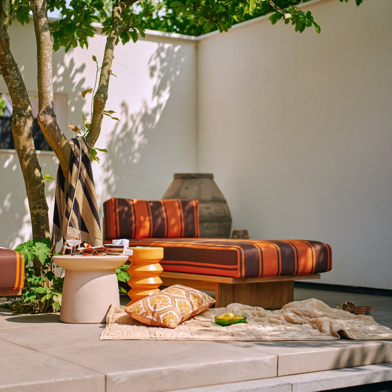 a pool side setting with earthenware and stoneware side table and stool with hkliving bowls and plates and hkliving style cushions and throws in browns and beige