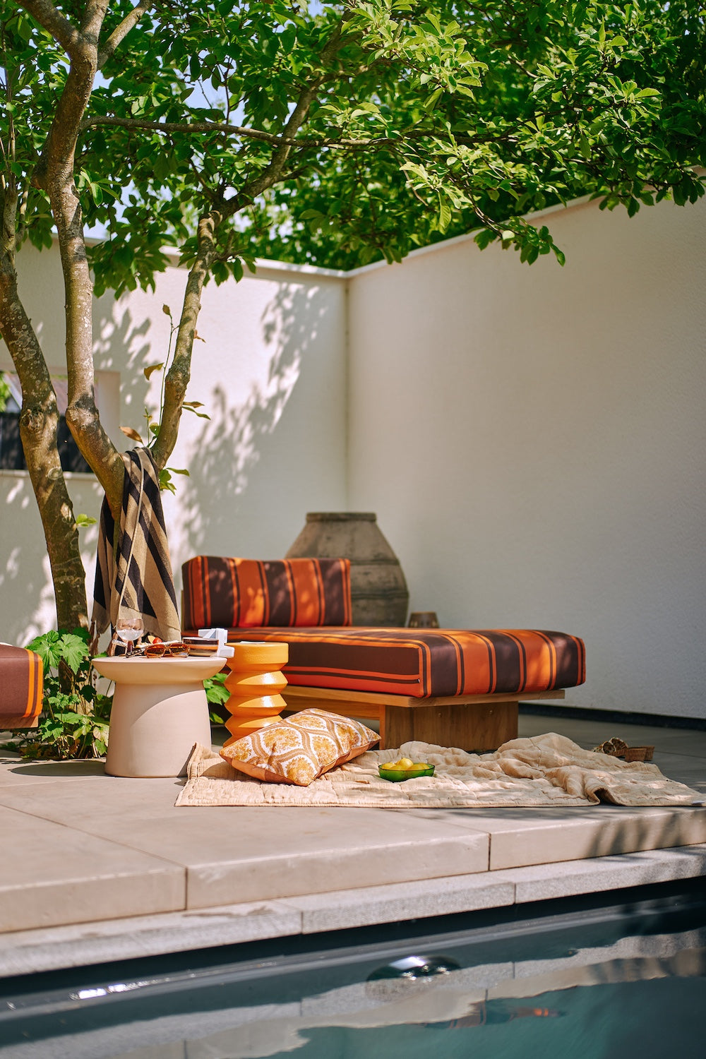 Terra stoneware side table by HKLIVING styled on a shaded outdoor terrace with striped daybed