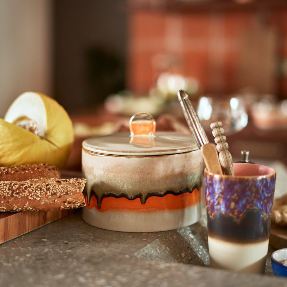 a cookie jar with the lid sat amongst other hkliving pottery pieces in a kitchen with sliced bread and melon