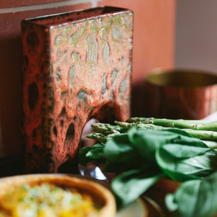 blocky vase with the look of lava where its all read but with blocks of red rising to the surface of its well laquered vase from hkliving surrounded by asparagus and basil