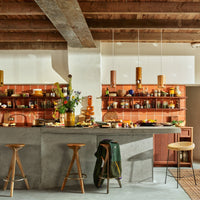 a kitchen with concrete worktops and wicker barstools filled with hkliving crockery and light fixtures