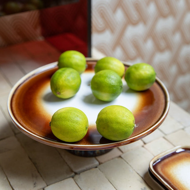 cake stand with green limes on a kitchen counter with a brown base and multi brown rim in hkliving colours