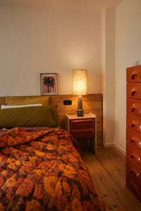 Stoneware lamp base by HKLIVING styled beside a floral bedspread and framed palm print artwork