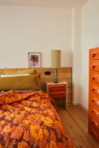 Stoneware lamp base by HKLIVING lit on an orange 70s-style bedside table in a colourful bedroom