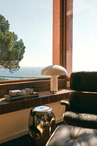 HKLIVING cream lounge table lamp on a brick windowsill overlooking the sea, beside a leather Eames-style chair