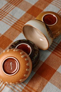 The undersides of four HKLIVING Drift tapas bowls turned over to show their differing base glazes and the hkliving stamp, arranged on an orange checked tablecloth