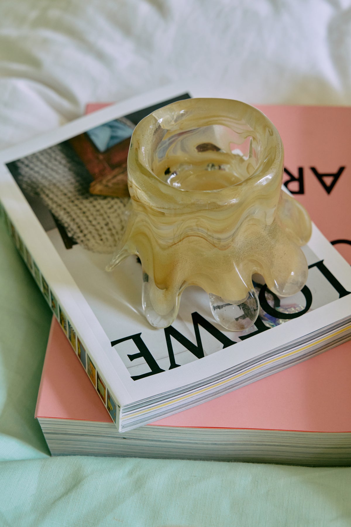 HKLIVING Melting Glass Candle Holder in Cream styled on a glass side table beside a bed, with a vase of yellow tulips and a large abstract painting behind