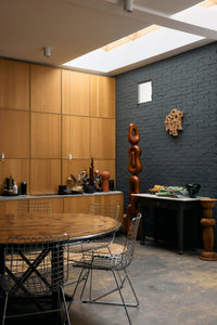 Dining room with timber-panelled walls and a round table, with the HKLIVING brutalist wall sculpture on the far wall