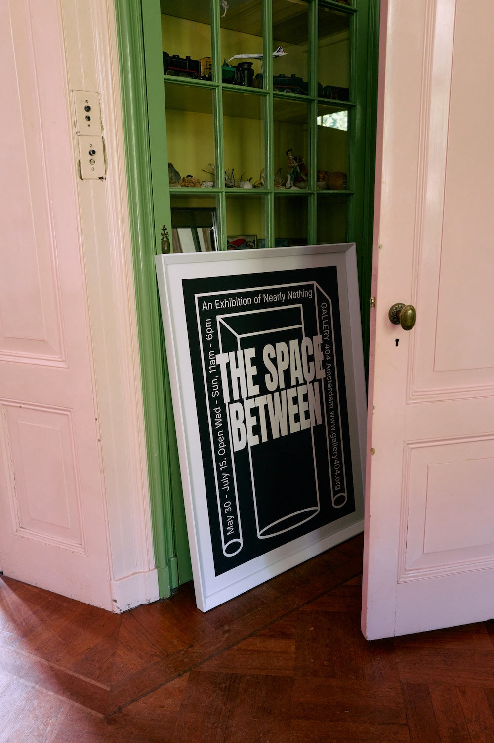 Between Space framed poster by HKLIVING propped inside a glass-fronted green cabinet doorway