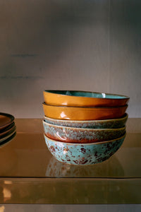 Two turquoise Patina 70s Ceramics pasta bowls by HKLIVING, with a warm tan glazed interior and rust-speckled exterior, stacked beneath bowls in other colourways from the same collection