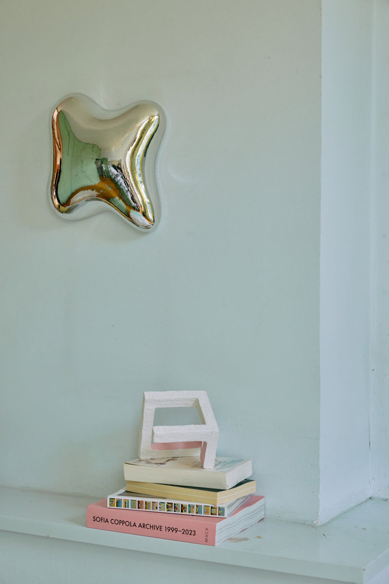 Chrome orb wall sculpture styled on a pale wall above stacked books and a small object