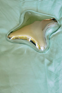 Metallic butterfly-shaped object on a light green fabric background