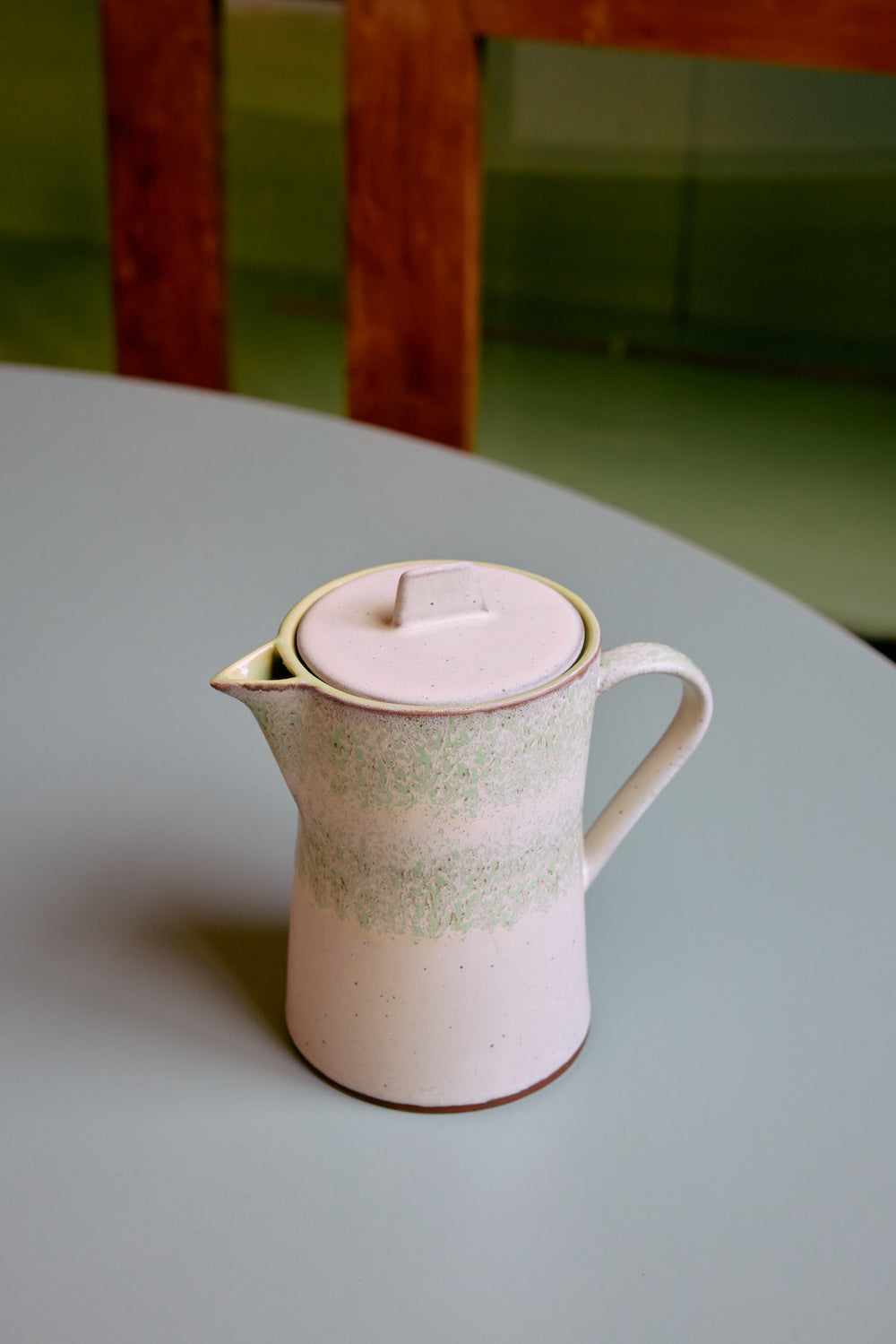 Cream stoneware teapot with a mottled sage green band from HKLIVING's 70s Ceramics collection in Slush, styled on a pale blue table
