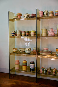 70s Ceramics storage jars from HKLIVING's collection displayed alongside mugs, bowls and a teapot from the same range on a glass shelving unit