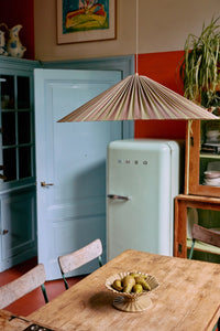 Large pleated Plisse pendant lamp in green and brown (Verdura) by HKLIVING, hung above a wooden dining table in a characterful kitchen with a pale green fridge