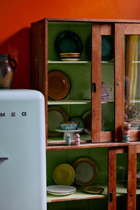 70s Ceramics pasta bowls in Patina displayed in a wooden cabinet alongside plates and mugs from HKLIVING's collection, beside a pale green fridge
