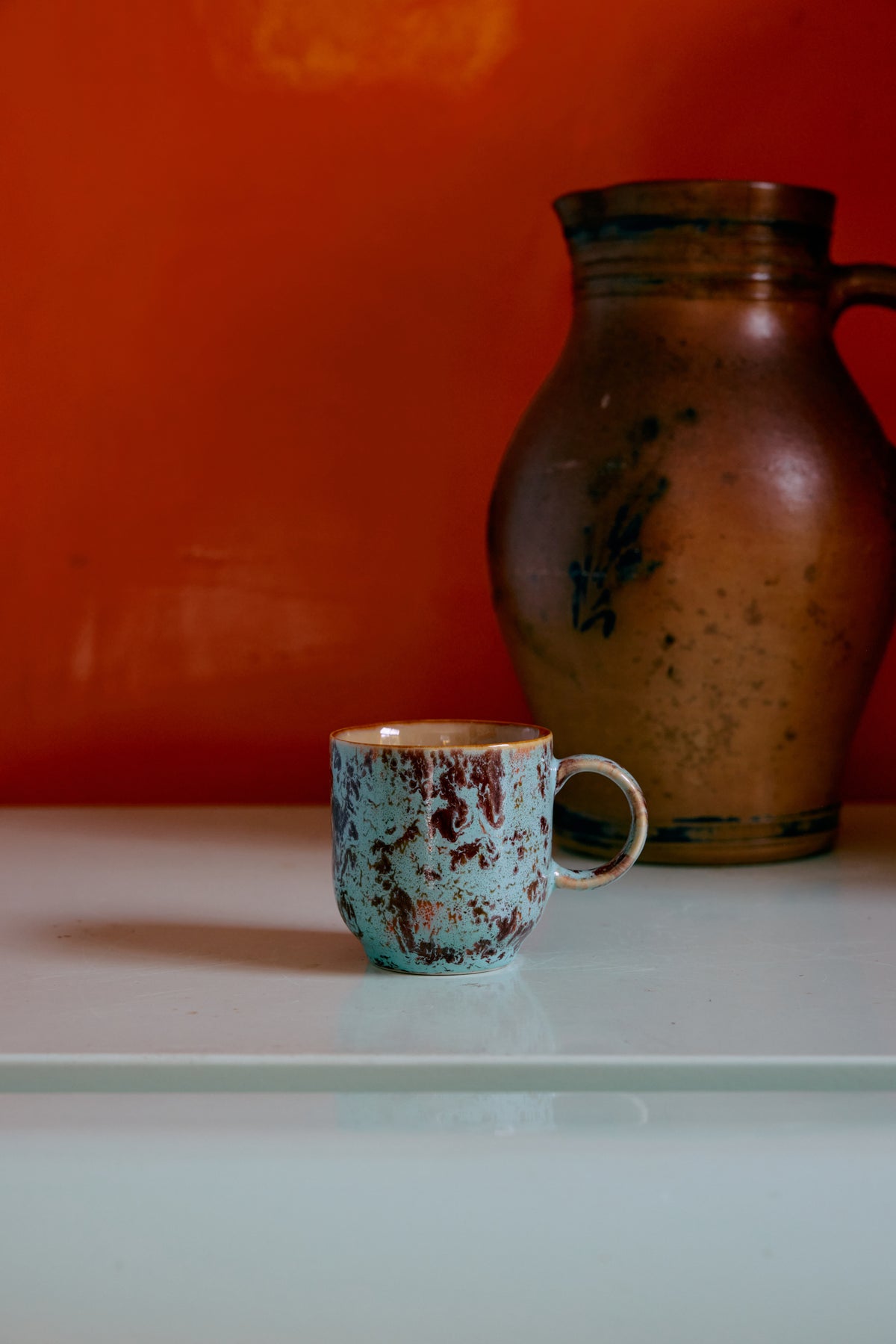Ceramic blue and brown mug and pitcher on a white surface with an orange wall background