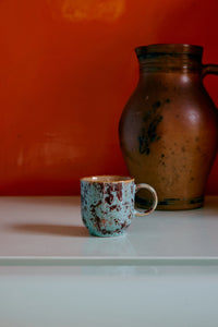 Ceramic blue and brown mug and pitcher on a white surface with an orange wall background