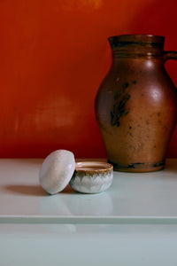 70s Ceramics sugar pot in Petal shown open with its lid resting beside it, styled next to a rustic stoneware pitcher against an orange wall